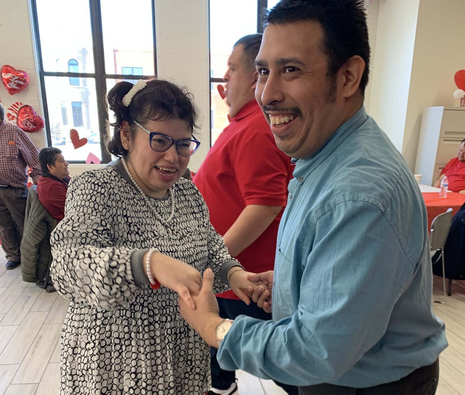 A man and a woman smile and hold hands at an El Valor celebration decorated with hearts.