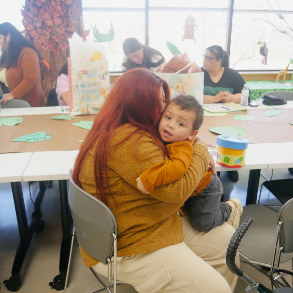 A woman hugs a young child at a classroom table.