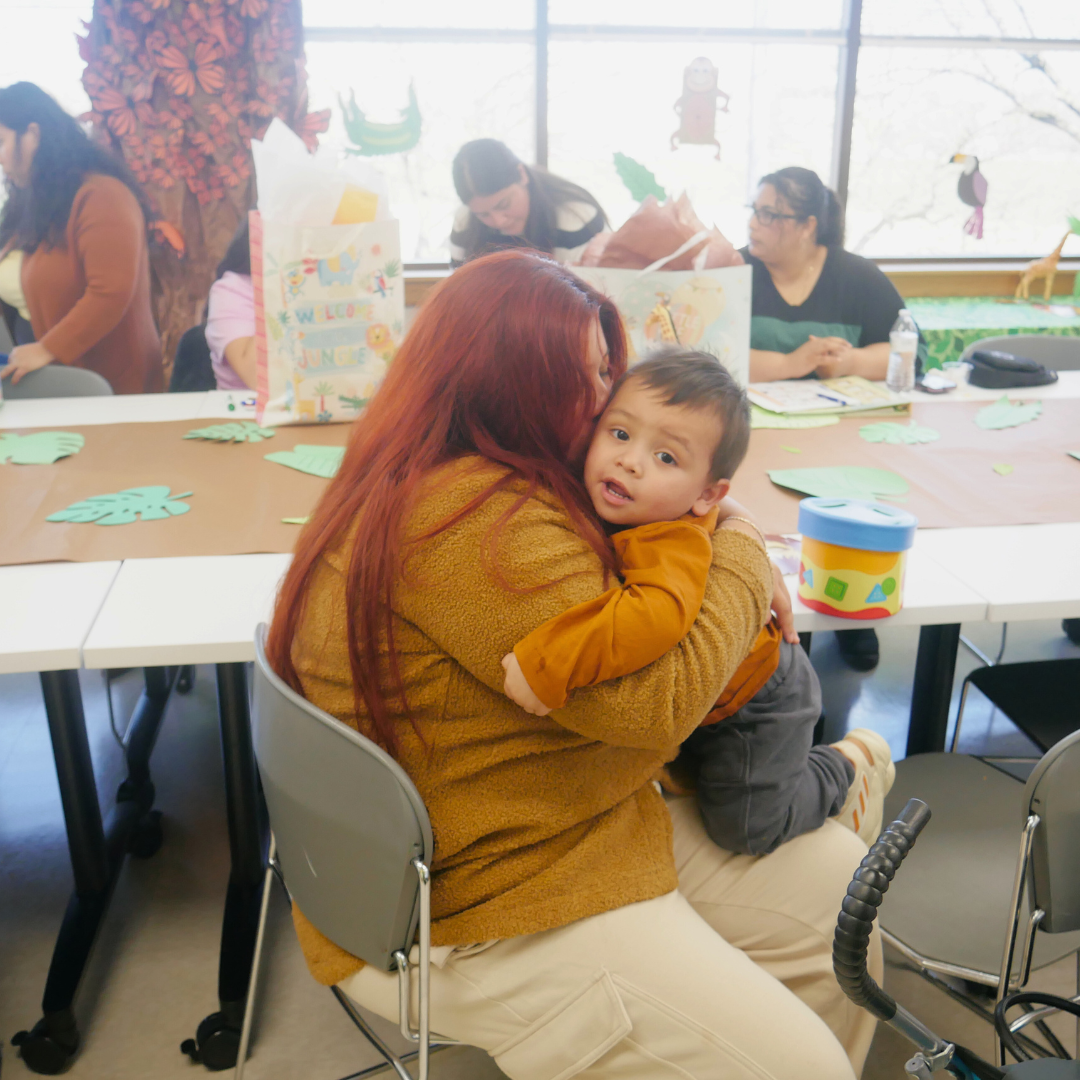 A woman hugs a young child at a classroom table.