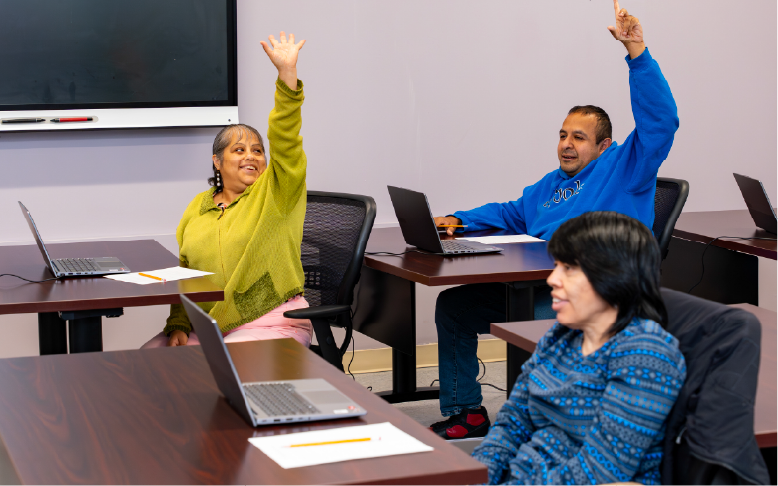 Adults raising their hands in an El Valor classroom