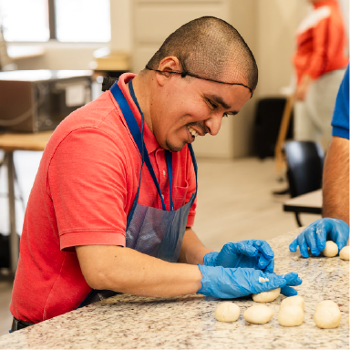 A man wearing an apron and gloves prepares dough in a kitchen.