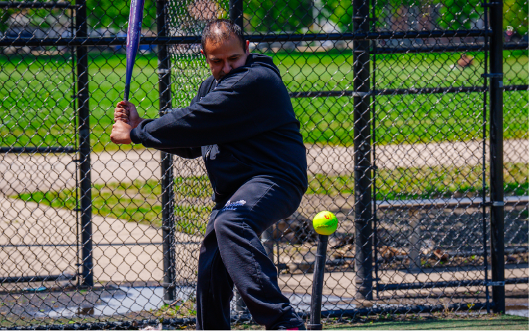 Adult in an El Valor sweater swinging a baseball bat