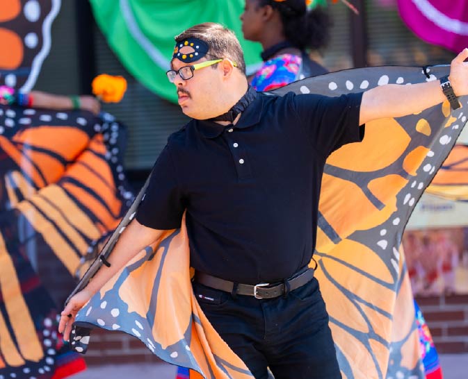 A man wearing large monarch butterfly wings performs a dance.