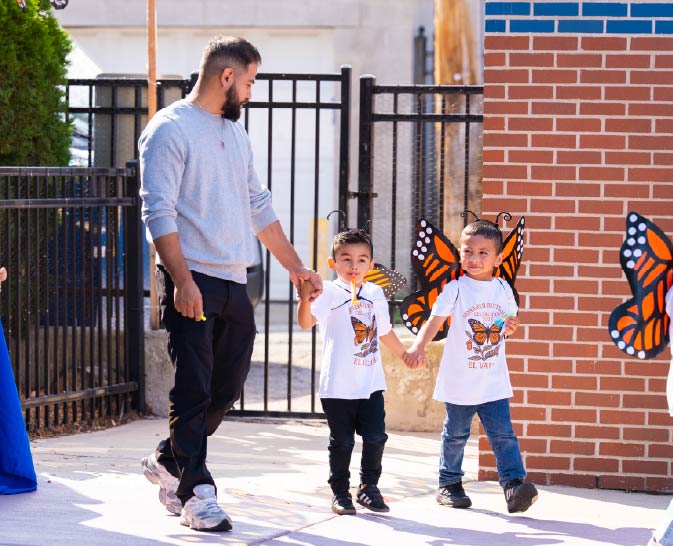A man walks hand in hand with two children wearing monarch butterfly wings at an El Valor event.