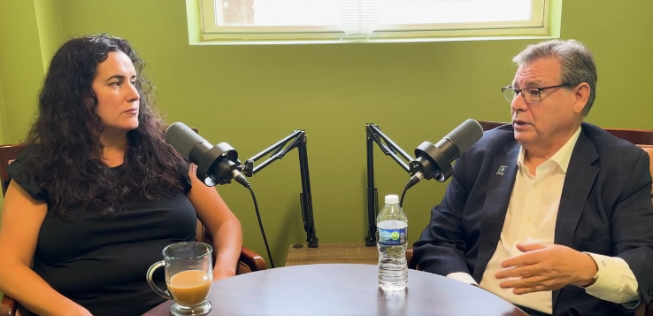 Two people speak at a table with microphones during an interview.