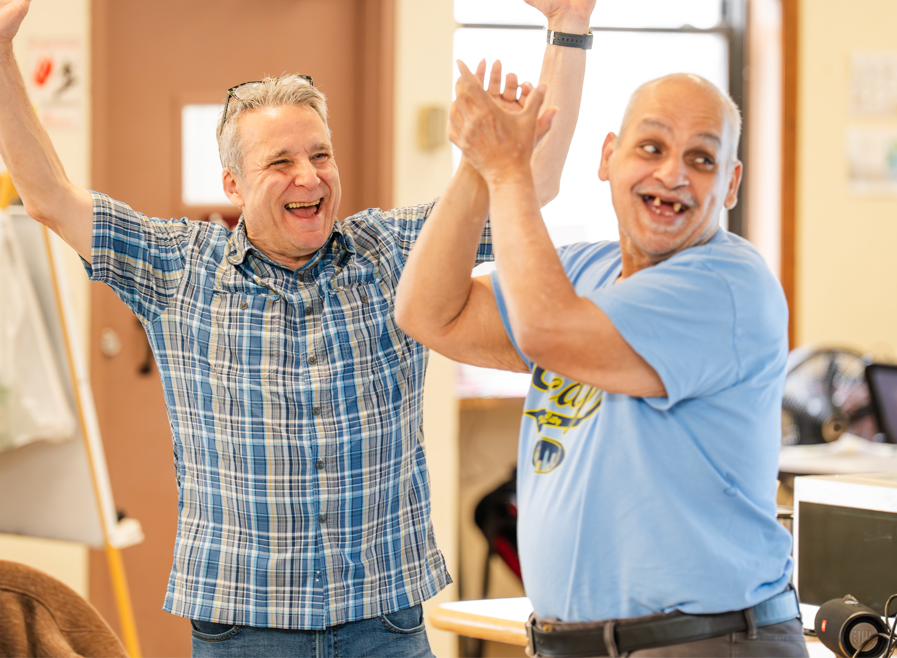 Two men celebrate together with raised arms and big smiles at an El Valor program.